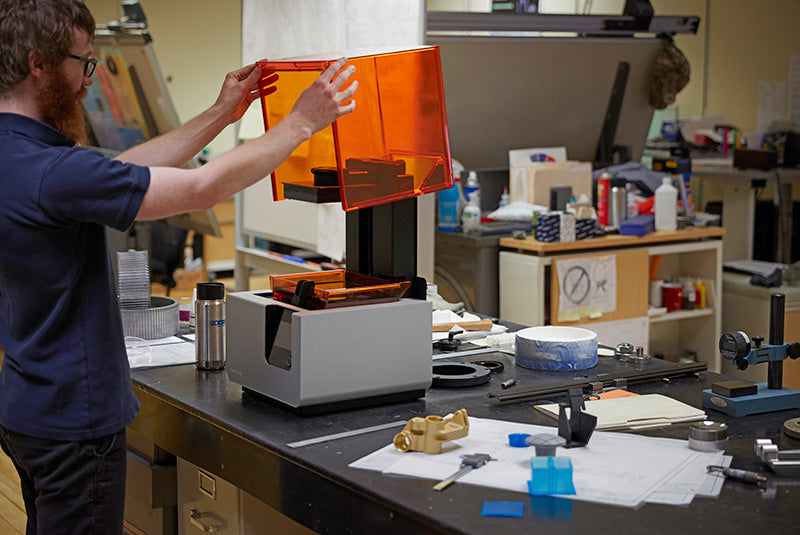 Man opening up 3D printer in workshop.